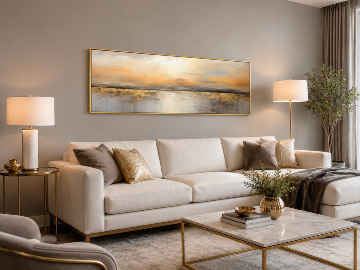 Long horizontal gold and silver abstract ocean sunset wall art hanging above a white sofa.