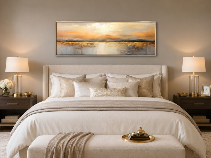 Long horizontal gold and silver ocean sunset abstract painting in a gold frame above a bed.