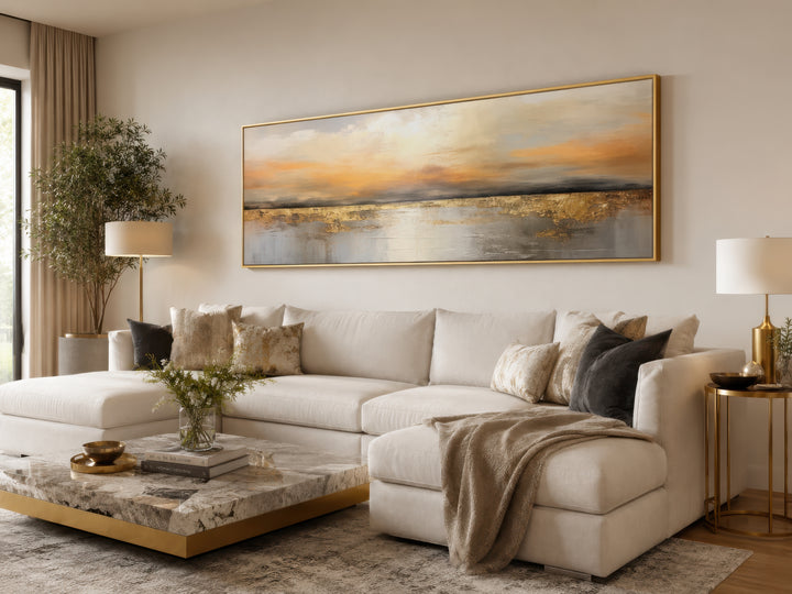 Gold and silver ocean sunset long horizontal wall art in a gold frame above a white sectional sofa.