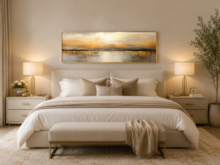 Long horizontal gold and silver abstract ocean sunset wall art hanging above a bed in a bedroom.