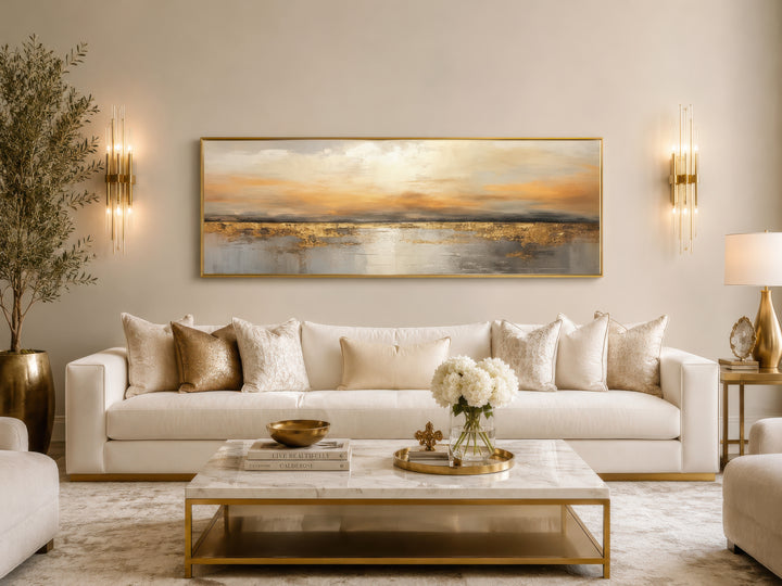 Long horizontal gold and silver abstract ocean sunset wall art hanging above a white sofa.