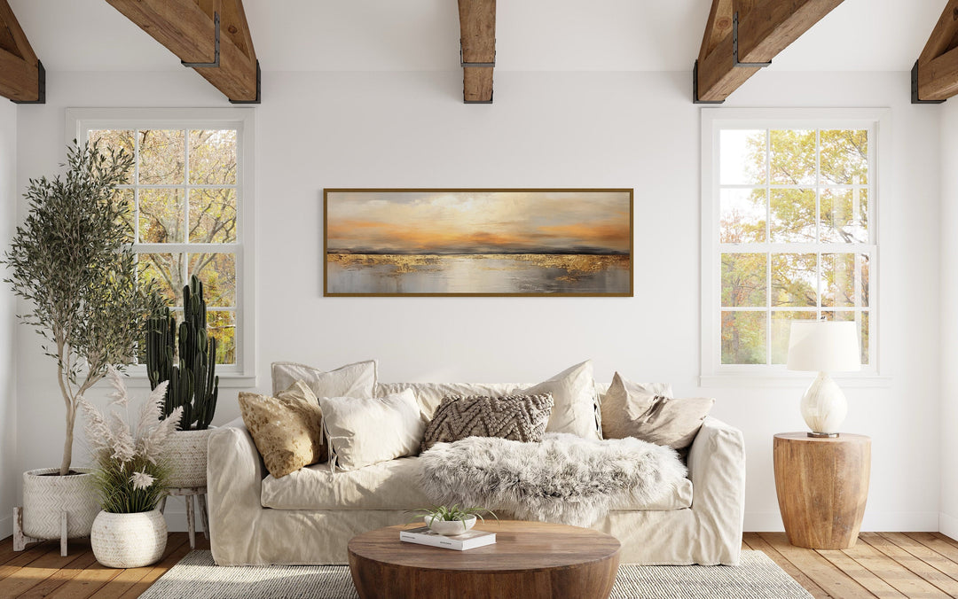 Gold and silver ocean sunset long horizontal wall art hanging above a beige sofa in a living room.