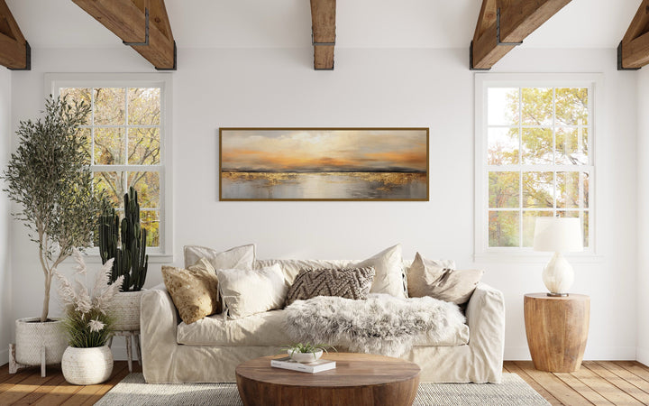 Gold and silver ocean sunset long horizontal wall art hanging above a beige sofa in a living room.