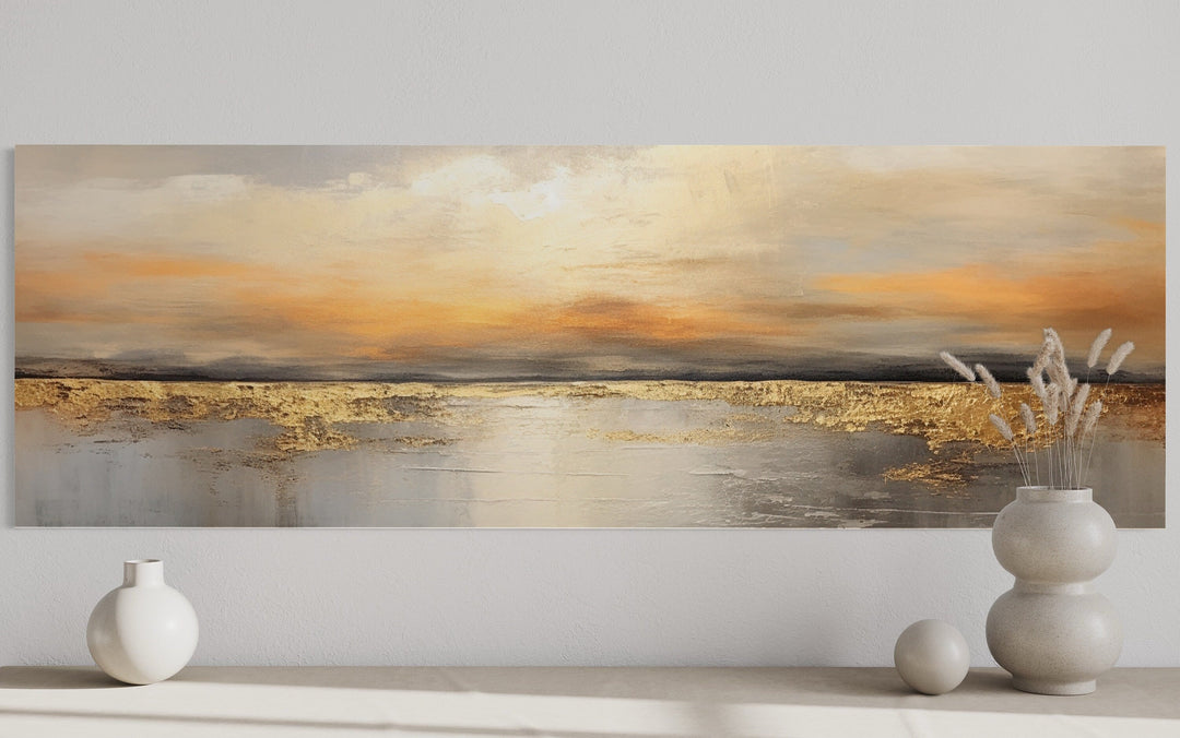 Long horizontal abstract wall art of a gold and silver ocean sunset above a white shelf.