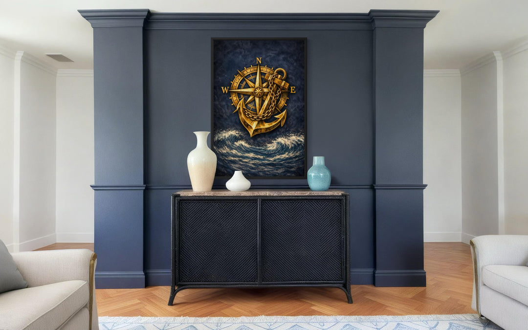 Gold compass and anchor canvas wall art centered on a dark navy blue wall above a black cabinet.