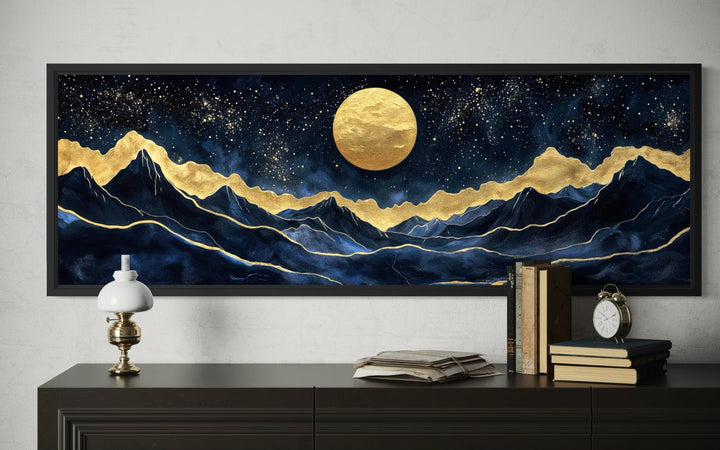 Panoramic canvas print of a gold moon over navy mountains with gold accents in a black frame.