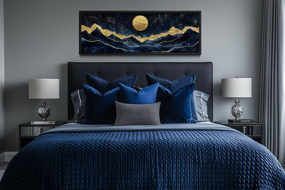 Panoramic canvas print of a gold moon over navy mountains hanging above a modern bed.