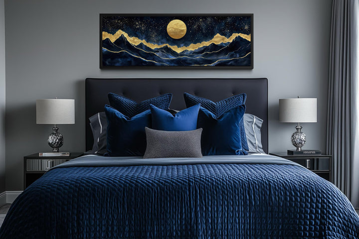 Panoramic canvas print of a gold moon over navy mountains hanging above a modern bed.