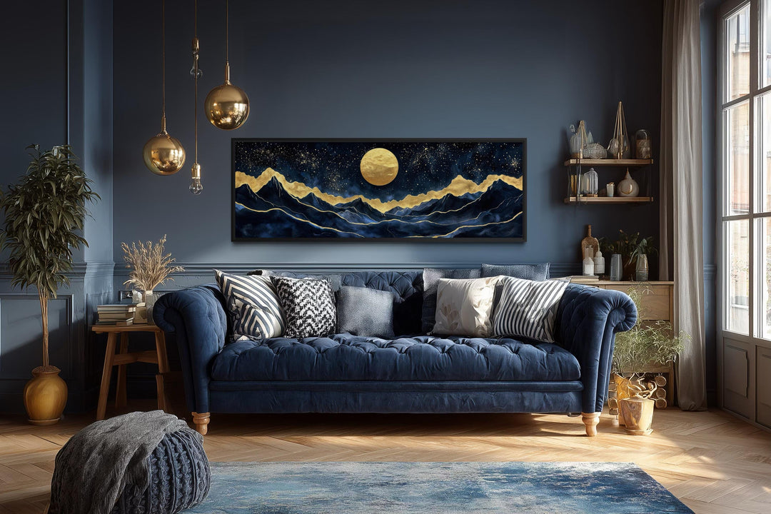 Panoramic gold and navy canvas print of a moonlit mountain landscape above a blue velvet sofa.