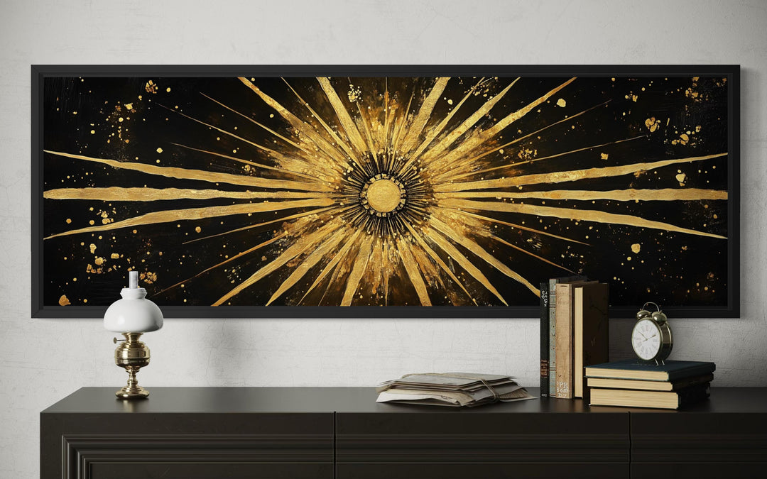 Horizontal black and gold sunburst abstract canvas painting above a dark sideboard.
