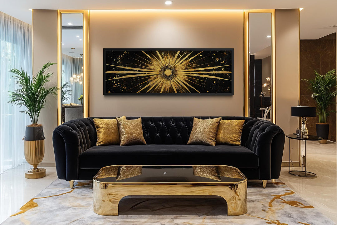 A long horizontal black and gold sunburst abstract painting hangs above a black velvet sofa.