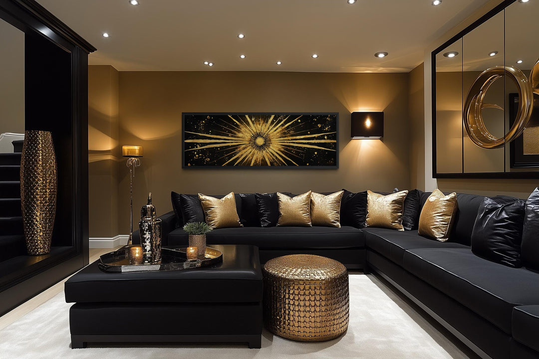 A long horizontal black and gold canvas painting of a radiant sunburst above a black sectional sofa.