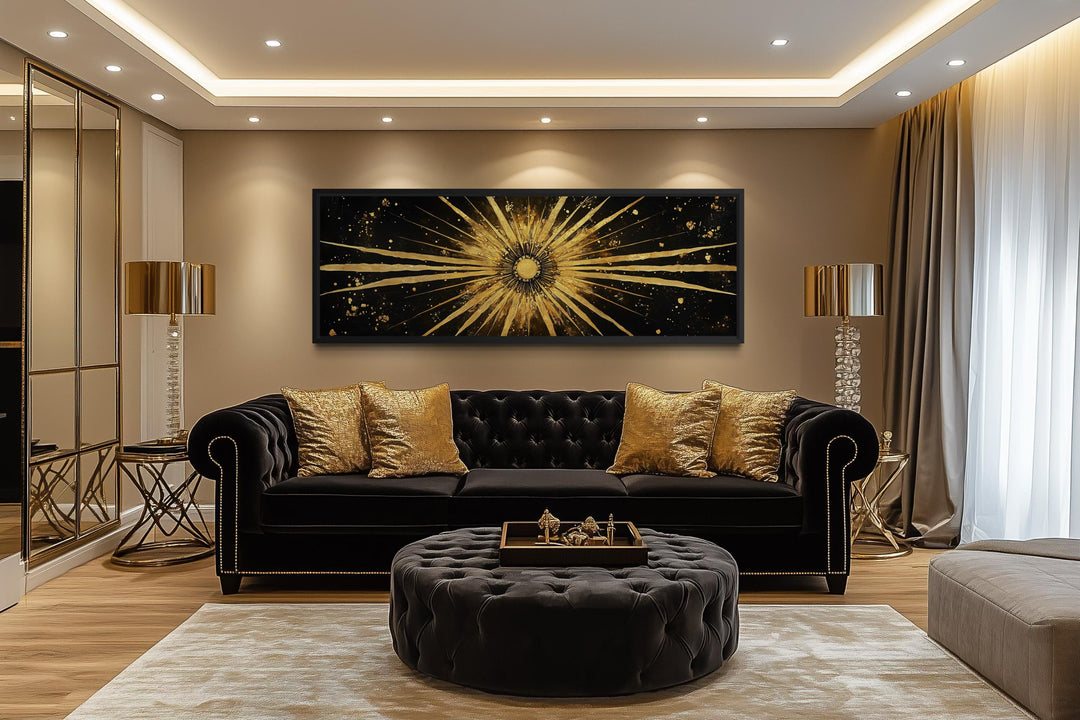 A long horizontal black and gold canvas painting of a radiant sunburst above a black velvet sofa.