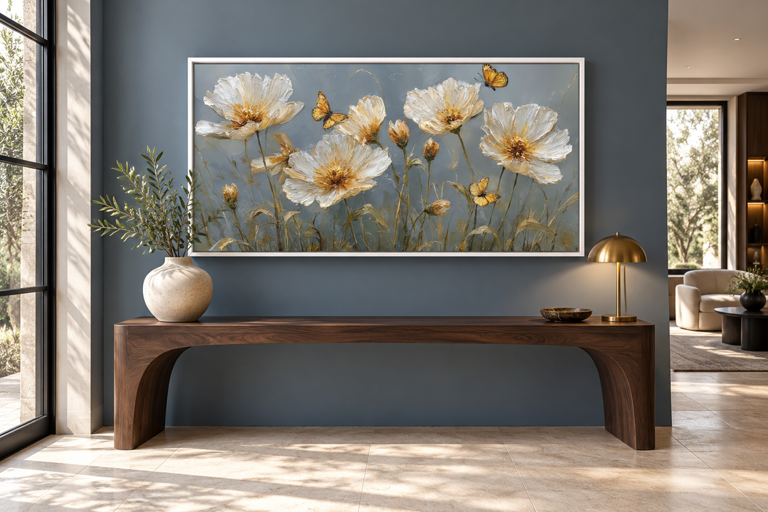Framed horizontal wall art of white and gold flowers with butterflies above a wooden console table.