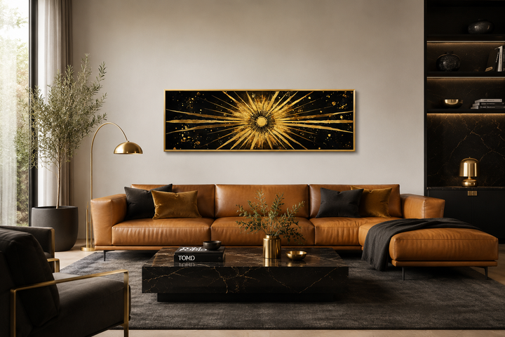 Long horizontal black and gold canvas wall art with a radiant sunburst above a leather sofa.