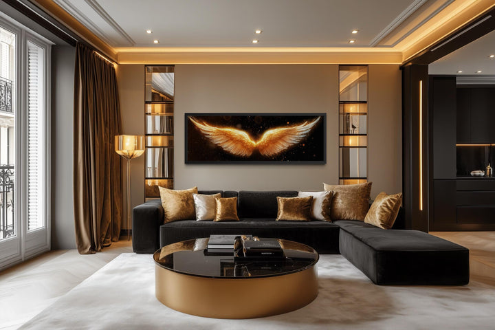 Horizontal canvas print of glowing golden angel wings centered above a black velvet sectional sofa.
