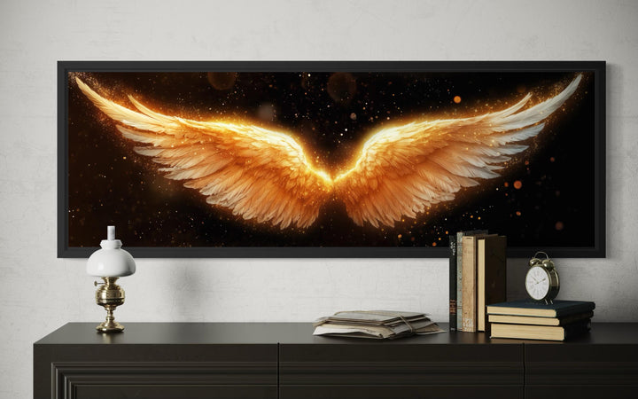 Horizontal canvas print of glowing golden angel wings on a black background in a black frame.