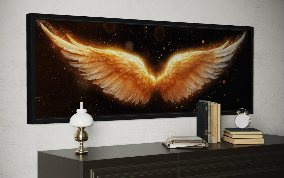 Horizontal canvas print of glowing golden angel wings on a black background in a black frame.