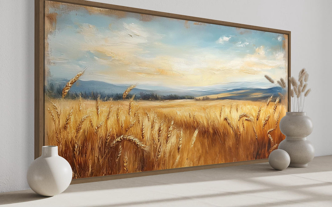 Golden wheat field farmhouse canvas wall art in a wooden frame above a neutral surface with vases.