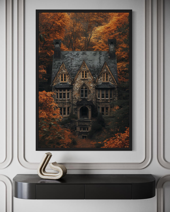 Gothic haunted house canvas art in a black frame above a console table with autumn forest backdrop.