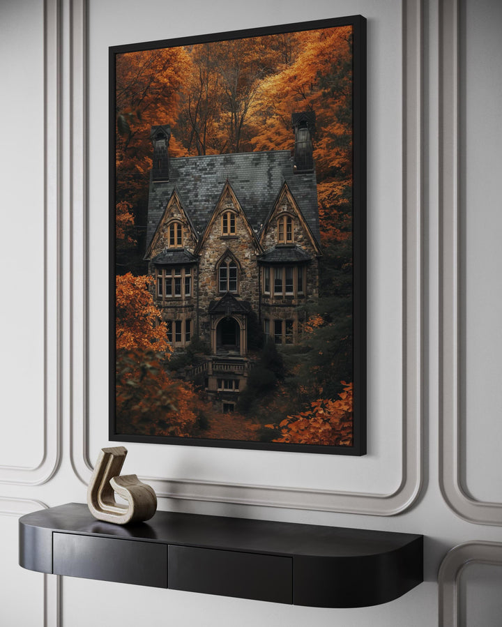 Gothic haunted house canvas art in a black frame above a console table with autumn forest backdrop.
