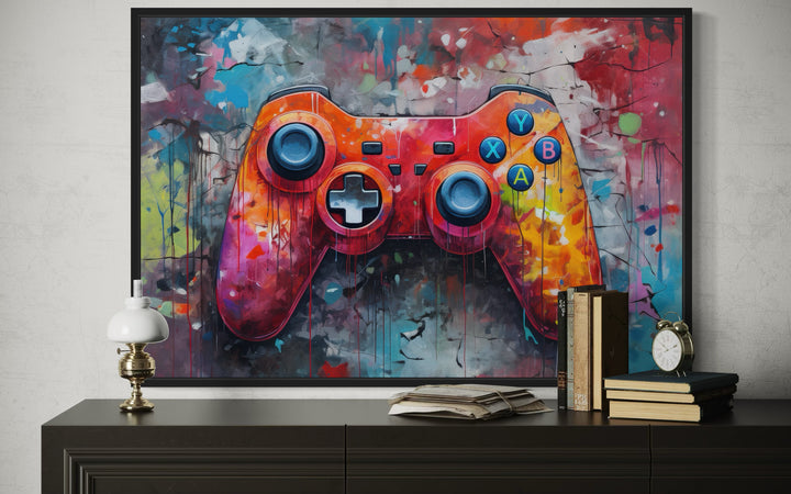 Framed graffiti-style canvas art of a colorful game controller hanging above a dark wood console.