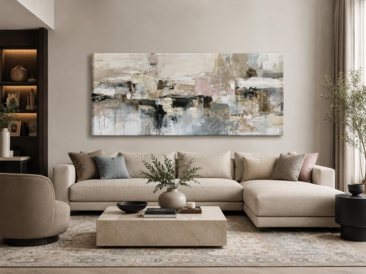 Horizontal abstract canvas print with gray, beige, and blush brushstrokes above a neutral sofa.