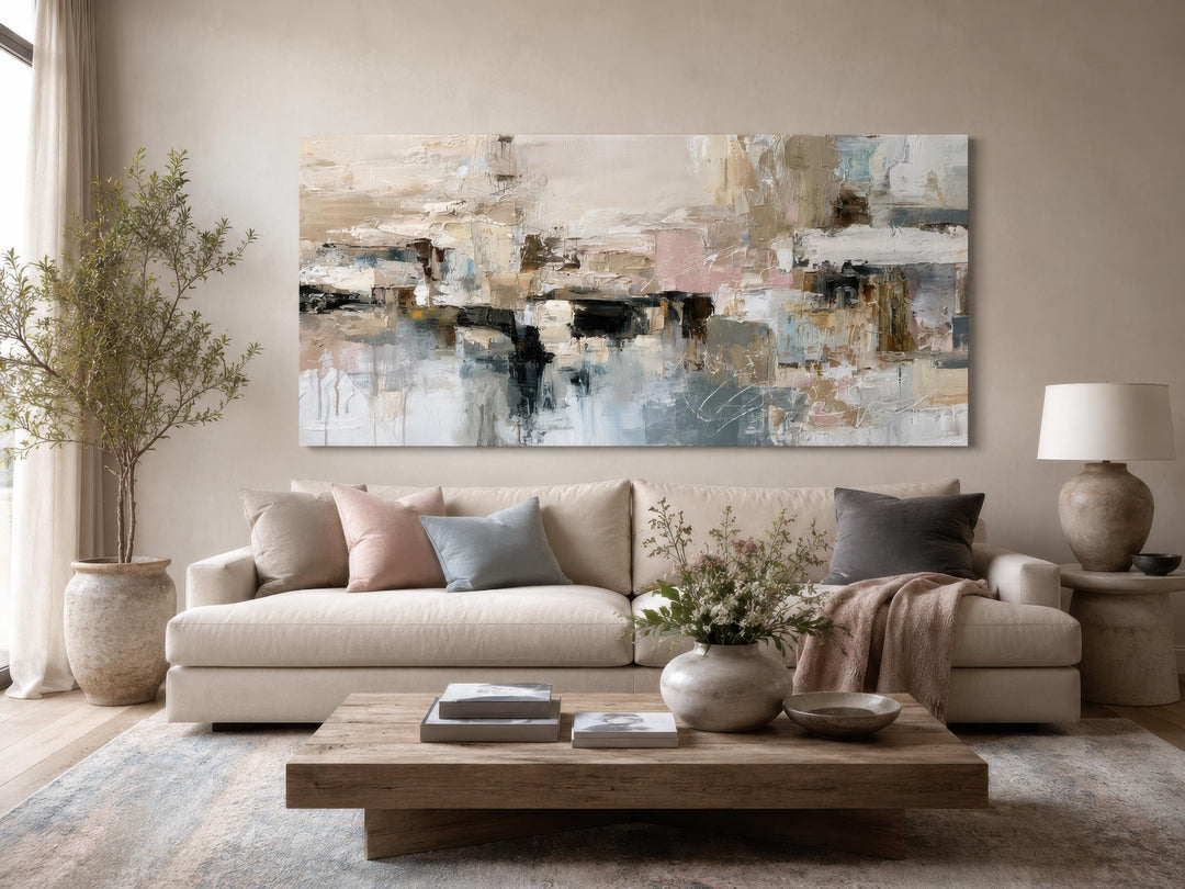 Horizontal abstract canvas print with gray, beige, and blush brushstrokes above a neutral sofa.