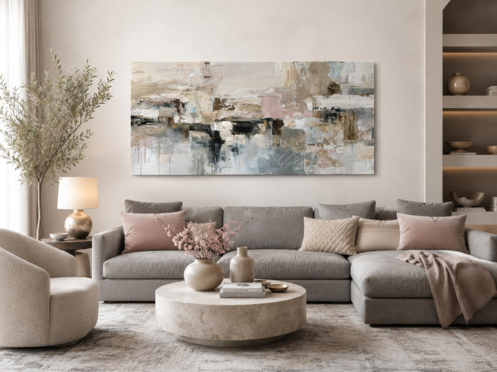 Horizontal abstract canvas print with gray, beige, and blush tones above a modern gray sofa.