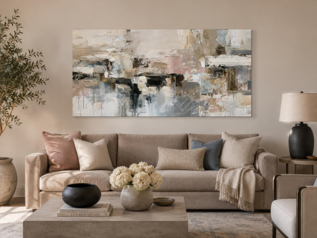 Horizontal abstract canvas print with gray, beige, and blush tones hanging above a neutral sofa.