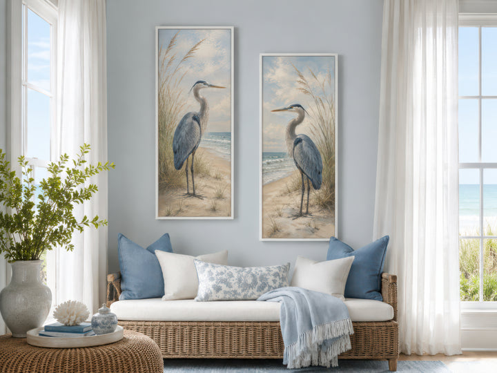 a living room with a wicker sofa, a coffee table, and two framed paintings of a heron on the wall. The room has a coastal theme, with a view of the ocean through the window.
