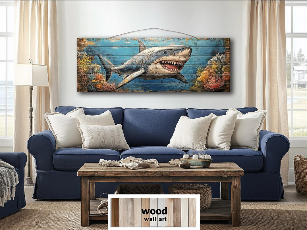 Horizontal wood wall art of a great white shark in a coral reef hanging above a blue sofa.