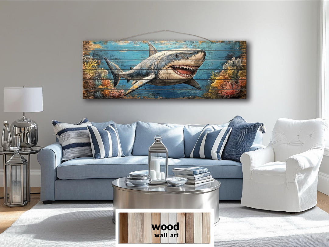 Horizontal wood wall art of a great white shark swimming through a coral reef above a blue sofa.