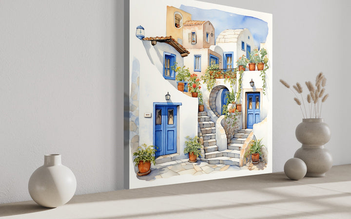 Watercolor canvas art of Santorini's white houses with blue doors and potted plants on a wall.