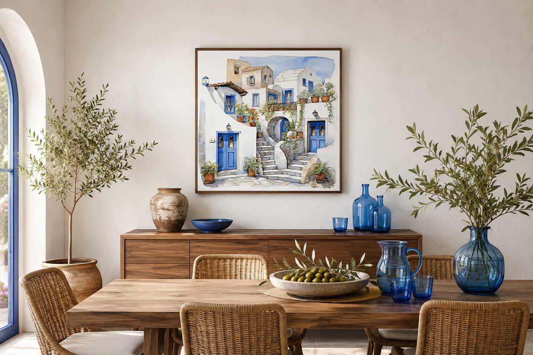 Framed watercolor canvas of Santorini's white houses and blue doors above a wooden dining table.