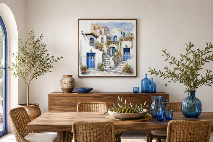 Framed watercolor canvas of Santorini's white houses and blue doors above a wooden dining table.