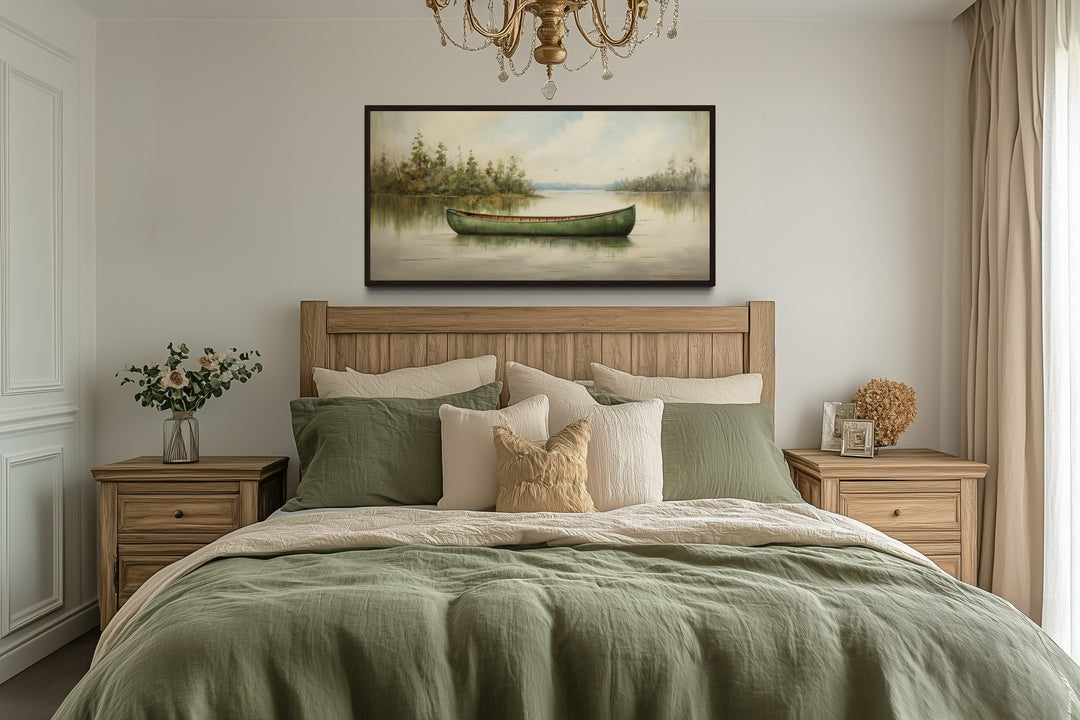Framed canvas painting of a green canoe on a calm lake, hung above a bed in a rustic bedroom.
