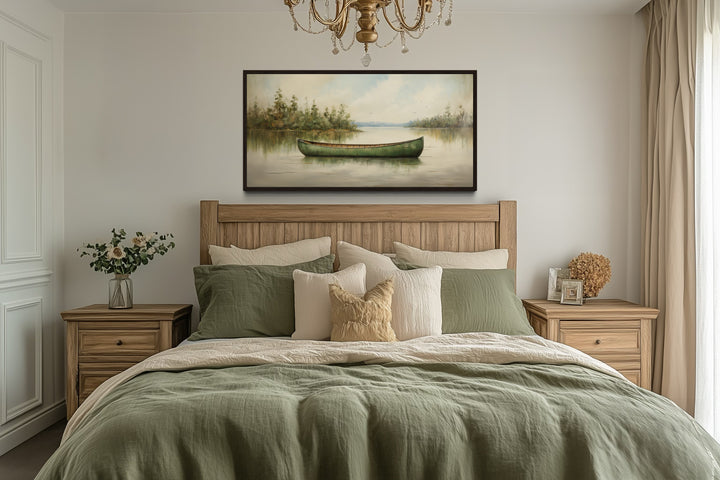 Framed canvas painting of a green canoe on a calm lake, hung above a bed in a rustic bedroom.