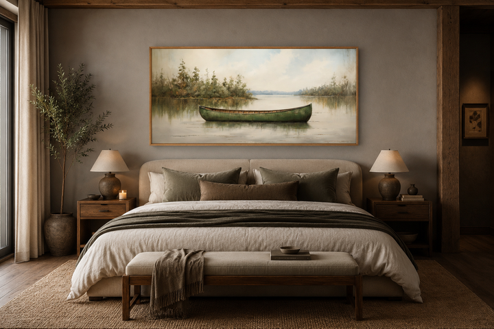 Framed wood canvas painting of a green canoe on a calm lake, hung above a bed in a rustic bedroom.