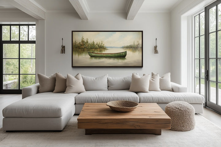Framed green canoe canvas painting on a calm lake, styled above a sofa in a rustic living room.