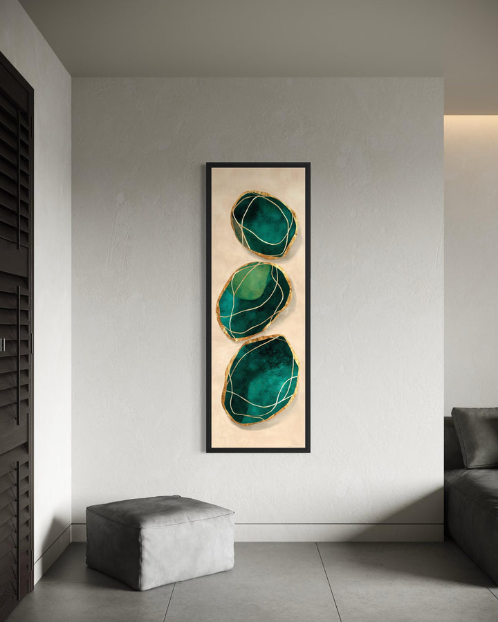 Vertical abstract painting of three emerald green stones with gold accents in a black frame.