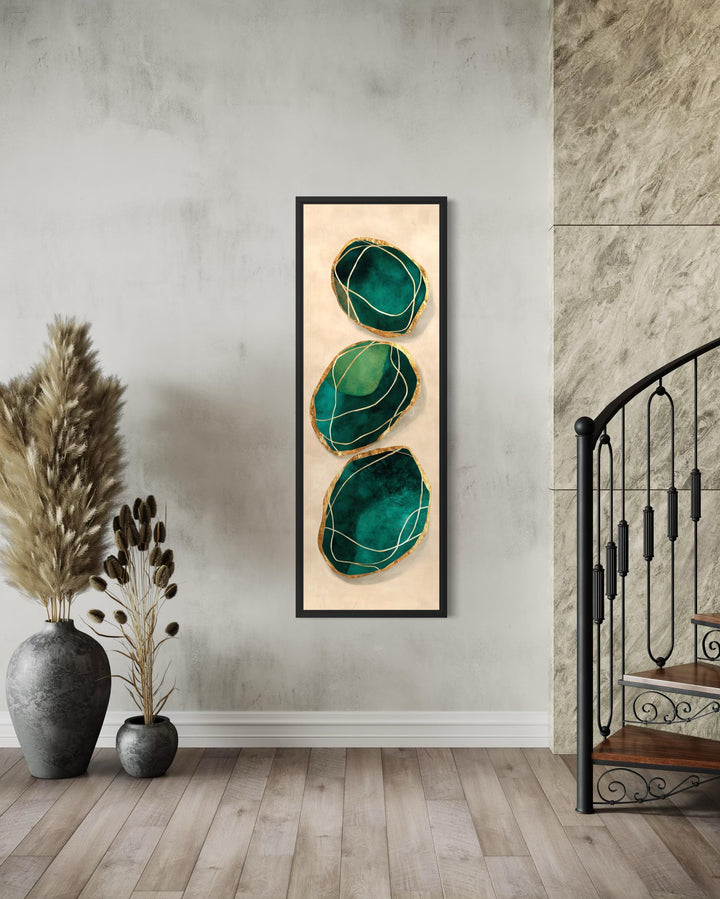 Vertical abstract wall art featuring three green and gold stones on a neutral canvas in a black frame.