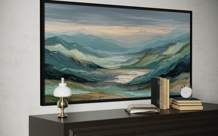 Green, grey, and gold mountain landscape wall art in a black frame above a dark wood console.