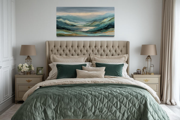Horizontal mountain landscape wall art in green, grey, and gold tones hanging above a tufted bed.