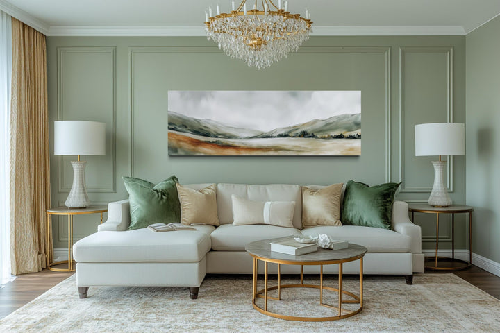 A panoramic canvas print of a minimalist green landscape hangs above a sofa in a sage-toned room.