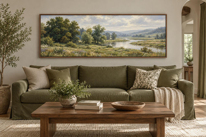 Green valley and river landscape long horizontal canvas wall art above a green sofa.