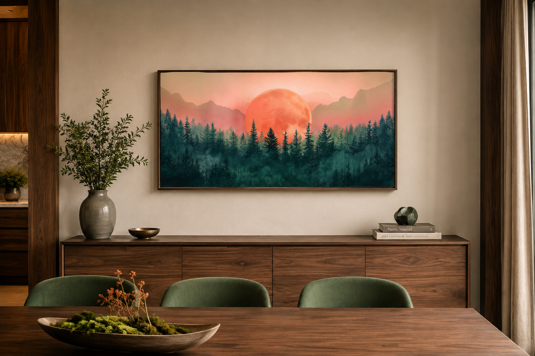 Framed canvas wall art of a pink sun setting over a green forest landscape above a wooden sideboard.
