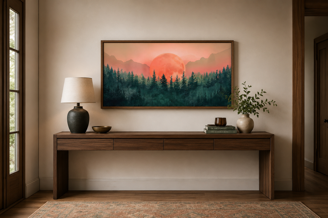 Framed horizontal canvas art of a pink sun setting over a green forest above a wooden console table.