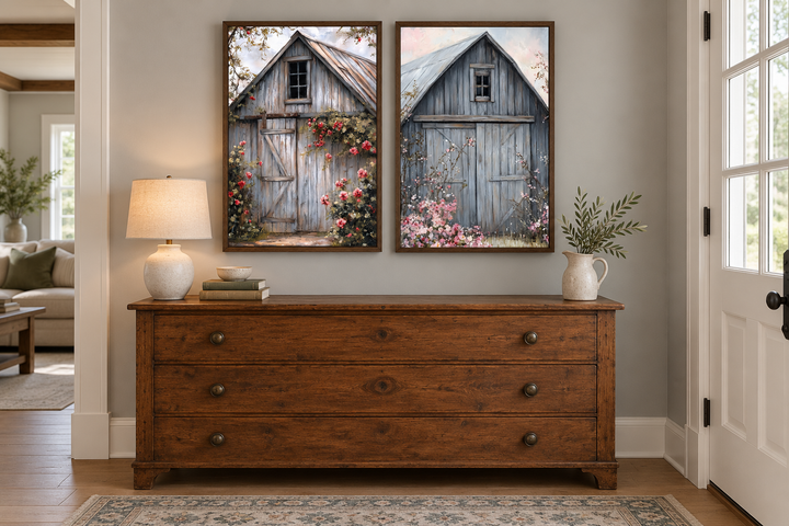Two framed canvas paintings of rustic grey barn doors with pink flowers above a wooden dresser.