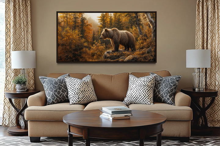 Framed canvas wall art of a grizzly bear in a golden autumn forest above a brown sofa.